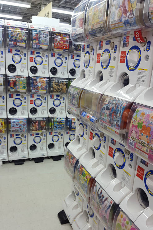 Gachapon vending machines in Japan filled with capsule toys and collectables, showing rows of colourful dispensers in an arcade or shop
