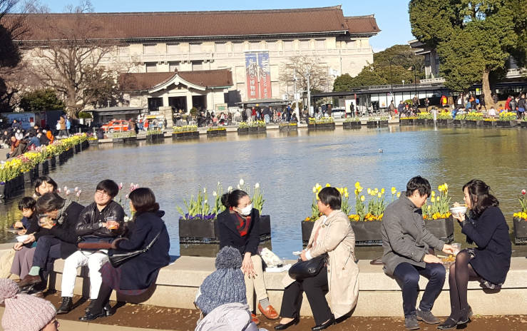 Small pond in Ueno Park, Tokyo, with people sitting along the edge and the Tokyo National Museum in the background during early spring