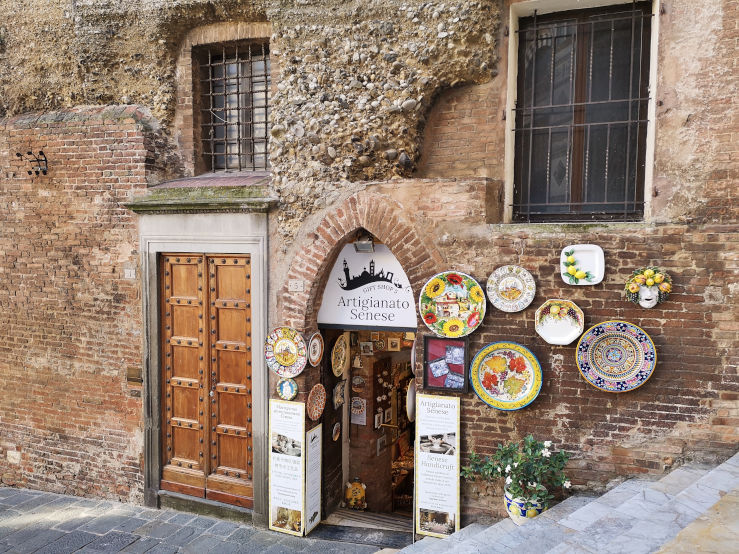 Artigianato Senese gift shop in a medieval building with an arched entrance and colourful ceramic plates in Siena