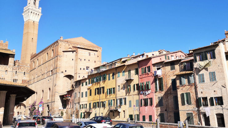 Colourful historic façades on Piazza del Mercato with Torre del Mangia rising above Siena's medieval skyline