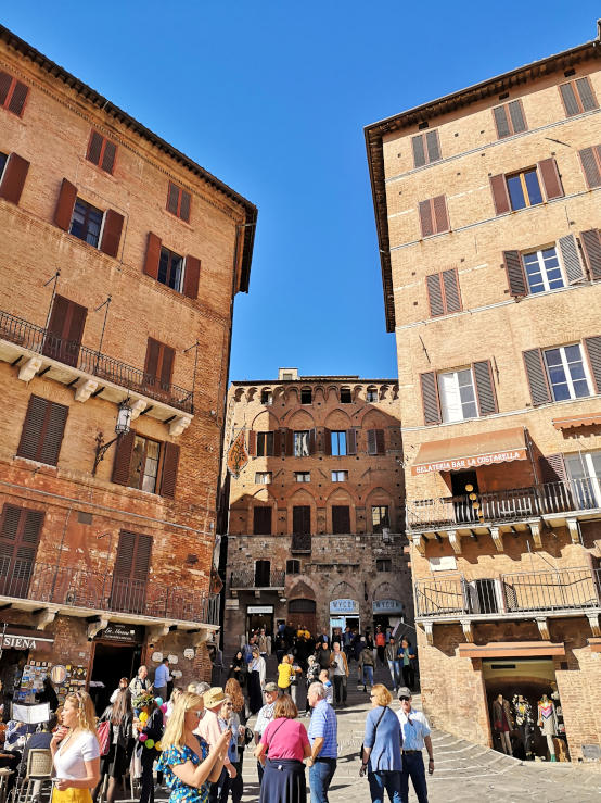 Visitors walking down a medieval side street towards Piazza del Campo in Siena's historic centre